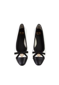 Ballerine in bianco e nero con punta arrotondata, punta in pelle nera, dettaglio con fiocco ed elemento decorativo dorato al centro.