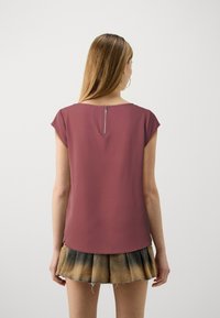 Haut à manches courtes bordeaux avec un col rond et un détail zip au dos. Tissu lisse avec une légère brillance.