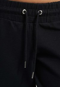 Czarne dresy o prążkowanej fakturze, z regulowanym sznurkiem w talii zakończonym srebrnymi metalowymi końcówkami i oczkami.