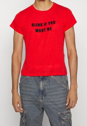 Punainen lyhythihainen t-paita, joka on valmistettu kevyestä kankaasta. Etupuolella on musta teksti printtinä, joka sanoo "BLINK IF YOU WANT ME".