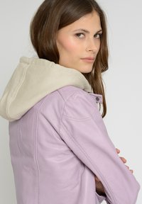 Lavendel læderjakke med en beige hætteforing, tætsiddende design og synlige syningsdetaljer. Har en trykknaplukning og sidelommer.