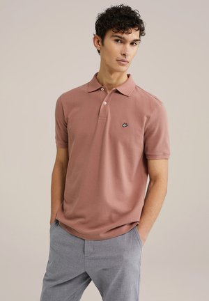 Helles rosa Polohemd aus Baumwolle, mit einem Kragen mit drei Knöpfen, kurzen Ärmeln und einem kleinen schwarzen und blauen Logo auf der Brust.