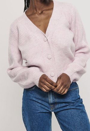 Lichtroze, geribbelde cardigan met een V-hals, drie grote knopen en lange mouwen, gecombineerd met een spijkerbroek met hoge taille.