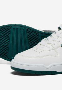 Sneaker bianco in pelle con punta perforata, suola in gomma verde con motivo testurizzato e lacci bianchi. Dettagli laterali in verde scuro.