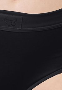 Schwarze, hochgeschnittene Unterhose aus einem glatten Stoff. Verfügt über einen mit Logo bestickten Bund und dezente Nähte.