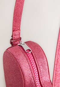 Pink glitter handbag with a rounded shape, featuring a shiny silver zipper, textured surface, and a thin, adjustable strap.