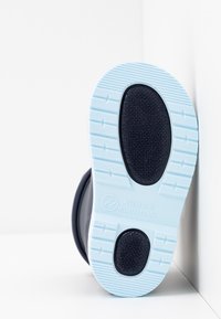 Semelle en caoutchouc avec une surface texturée bleu foncé, semelle extérieure bleu clair présentant des motifs de traction, et un texte gravé indiquant "Fabriqué en Espagne."