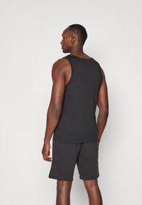 Svart tanktop laget av bomull, med en avslappet passform. Bakpå har den rund hals. Brukt med mørkegrå shorts, glatt tekstur.