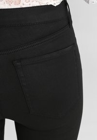 Jeans de mezclilla negra con una textura suave, cintura alta y detalles en los bolsillos traseros. Presenta un patrón de costura sutil y una silueta ajustada.