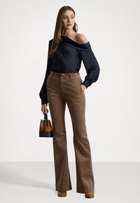 Marinemarine off-shoulder top met lange mouwen, bruine corduroy flared pants, tan riem met logo, en zwarte en bruine handtas met handvatten.