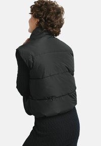 Czarna kamizelka puchowa z wysokim kołnierzem, charakteryzująca się pikowanym wzorem i szerokim, bezrękawnikowym krojem. Gładka tekstura i lekki wygląd.