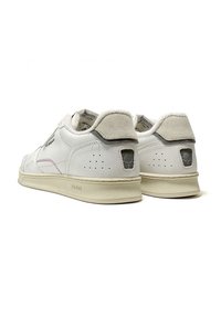 Sneaker bianche in pelle con un'etichetta posteriore testurizzata, dettagli perforati e una suola in gomma beige. Presentano un branding discreto e un colletto imbottito.