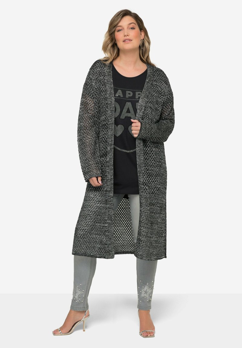 Dlouhý otevřený kardigan v černobíle pletené látce. Nosený přes černé grafikou potištěné tričko, spárovaný se šedými džíny se dekoračními nýty.