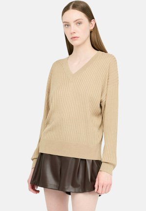 Maglione beige a scollo a V con trama a costine, maniche lunghe e vestibilità comoda, abbinato a una gonna in pelle sintetica marrone scuro.