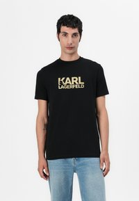 Camiseta de algodón negra con escote redondo y mangas cortas, que presenta el logotipo en dorado "KARL LAGERFELD" en el frente. Corte clásico.