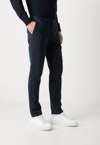 Navy chinos with a slim fit, featuring side pockets, a belt loop, and a smooth, durable fabric, paired with white sneakers.