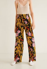 Pantaloni a gamba larga con motivo floreale nero, caratterizzati da foglie vivaci di colore rosa e giallo. Tessuto leggero con una vestibilità rilassata.