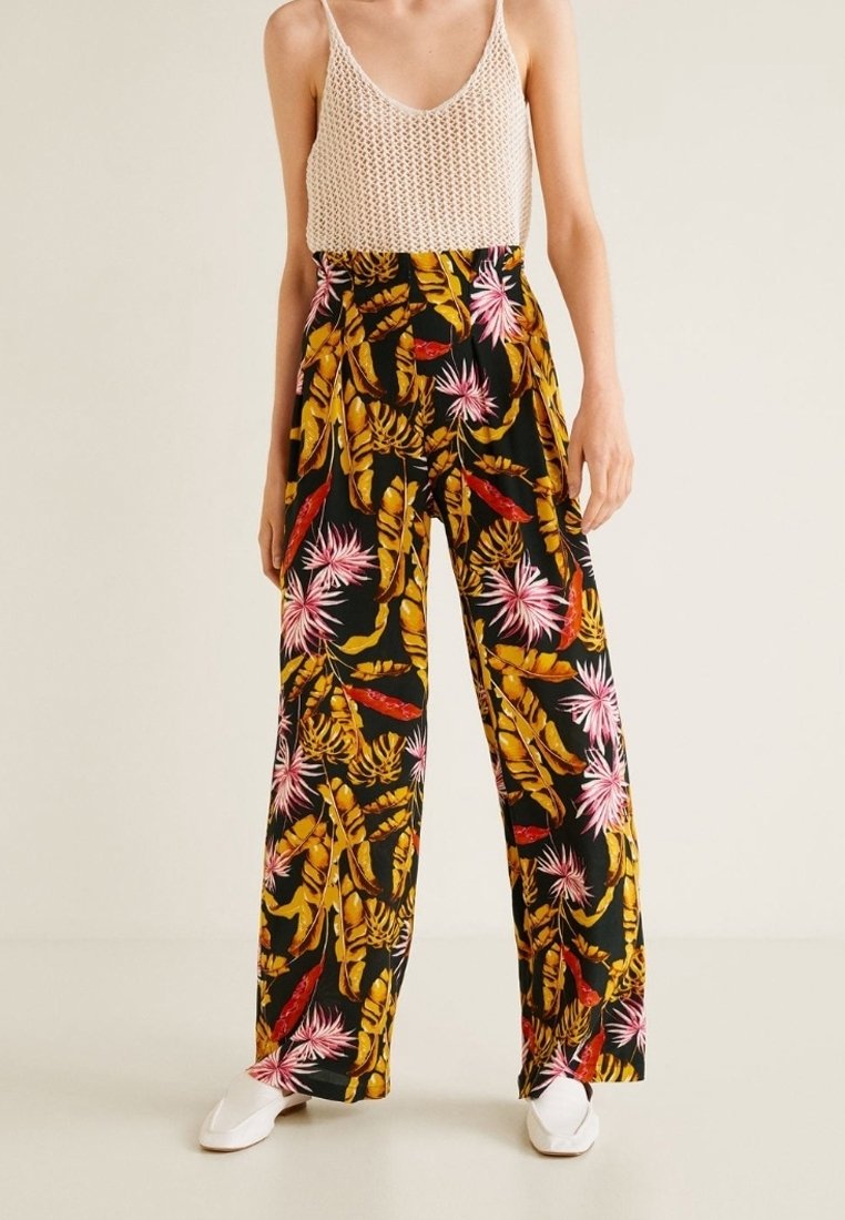 Pantaloni a gamba larga con motivo floreale nero, caratterizzati da foglie vivaci di colore rosa e giallo. Tessuto leggero con una vestibilità rilassata.