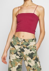 Mörkröd ribbad crop top med tunna remmar, ihop med beige och grön kamouflagebyxor. Anmärkningsvärda detaljer: figurnära design och kort längd.