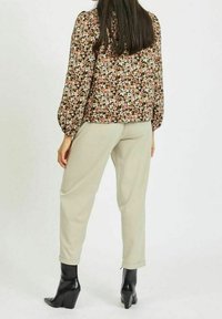 Blommig blus i mörkbrunt med rosa, vitt och grönt mönster; puffiga ärmar; kombinerat med ljusgröna byxor och svarta klackstövlar.