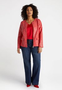 Röd paljettbombarjacka med dragkedja framtill, kombinerad med en röd topp och mörkblå vida byxor. Röda spetsiga skor kompletterar outfiten.