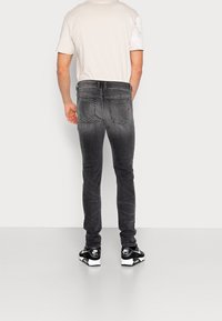 Jeans gris de corte slim con costuras en contraste, diseño de cinco bolsillos y un ligero desgaste, combinados con una camisa de color claro y zapatillas negras.