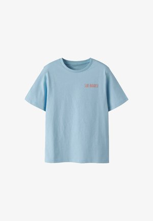 T-shirt bleu clair à manches courtes avec col rond et petit texte rouge "SURF PARADISE" sur le côté gauche de la poitrine.