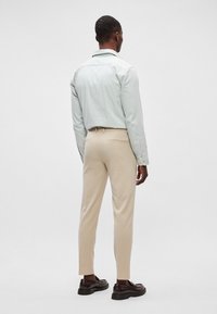 Ανοιχτό πράσινο πουκάμισο με χαλαρό γιακά, συνδυασμένο με κρεμ tapered παντελόνι και καφέ παπούτσια, εμφανίζεται από την πίσω πλευρά.