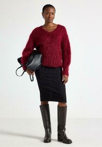 Viininpunainen, pörröinen neule V-pääntiellä, yhdistetty mustaan, teksturoituun kynähameeseen ja polven korkeisiin ruskeisiin nahkasaappaisiin. Musta käsilaukku kädessä.