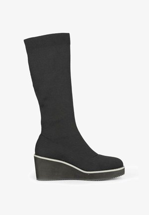 Bota de muslo negra de punto con una parte superior amplia y suave, puntera redondeada y suela de plataforma de cuña con un borde blanco en contraste.