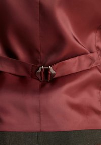 Maroon satenasti odjevni predmet s glatkom teksturom, koji ima dizajn s pojasom i metalnu kopču na struku.
