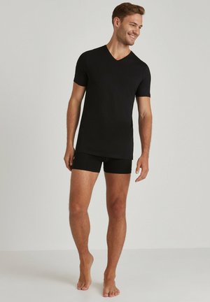 Czarna koszulka z dekoltem w kształcie litery V i krótkim rękawem, zestawiona z czarnymi dopasowanymi szortami. Materiał wygląda na gładki i lekki.