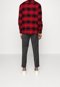 Camicia a quadri rossa e nera, maniche lunghe, abbinata a pantaloni grigi e sneakers bianche. Focus sul motivo a quadri e sulla vestibilità casual.