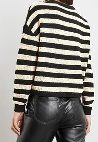 Schwarz-creme gestreifter Strickpullover mit Rundhalsausschnitt und geripptem Saum, kombiniert mit schwarzen Kunstlederhosen, die über eine Gesäßtasche verfügen.