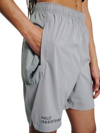 Osoba nosząca jasnoszare sportowe spodenki z elastycznym pasem i boczną kieszenią, ręka częściowo w kieszeni, tekst "HALO 196819721981" na krawędzi.
