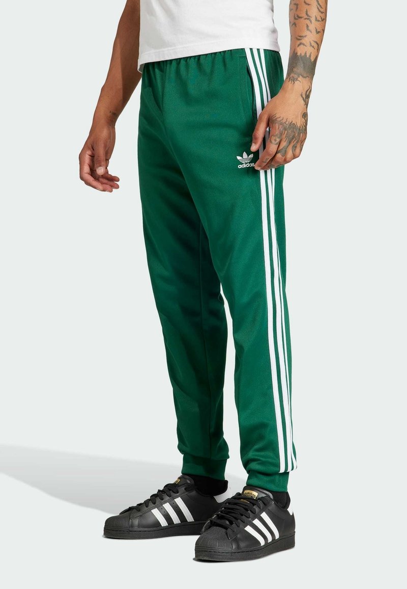 Zelené sportovní kalhoty s bílými postranními pruhy, vyrobené z hladké tkaniny, s elastickým pasem a malým logem na levém stehně.