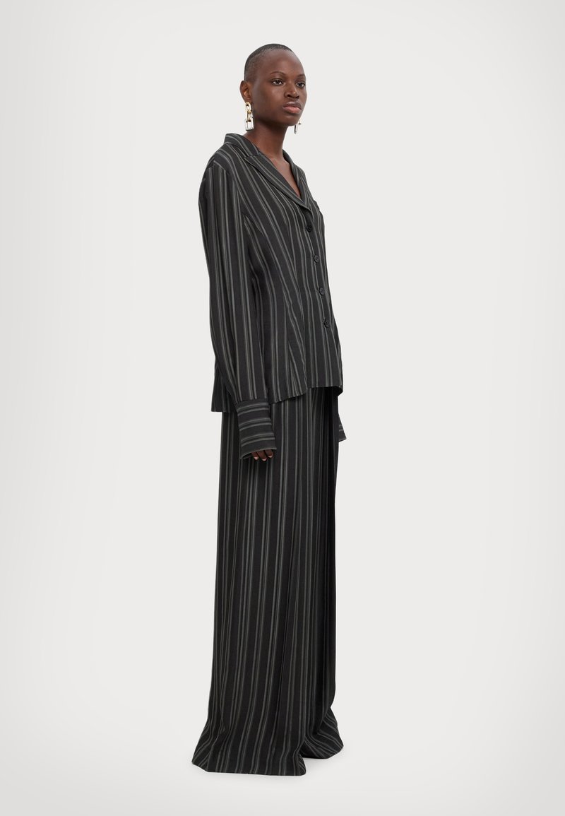 Black and gray striped pajama set made of soft fabric; features a long button-up shirt and wide-leg pants with a relaxed fit.