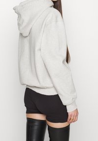 Světle šedá mikina s klokaní kapsou, žebrovanými manžetami a kapucí na šňůrku. Nosit s černými šortkami a černými botami do stehna.