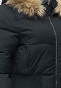 Μαύρο χειμωνιάτικο μπουφάν με επένδυση, μπροστινό φερμουάρ, πλαϊνές τσέπες, ριμπ ζώνη στη μέση και κουκούλα με γαλάζιο γούνα ψεύτικη γούνα.