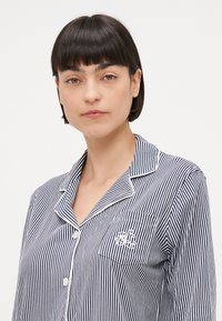 Randig pyjamaskjorta i marinblått och vitt, med en skör krage, knäppning fram och broderad fickdetalj. Tillverkad i bomull, avslappnad passform.