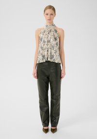 Top cu bretele din mărgele, cu un model bej și argintiu, asortat cu pantaloni de piele verzi închiși, ajustați, și tocuri maro cu vârf ascuțit.