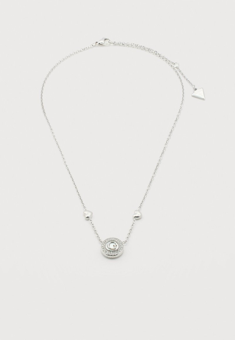 Collier en chaîne argentée avec un pendentif rond mettant en évidence un "G" central entouré de petits cristaux et deux perles en forme de cœur sur la chaîne.