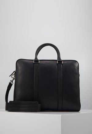 Malette en cuir noir avec deux poignées supérieures, sangle détachable, texture lisse et détails de couture verticale contrastante. Fermeture zippée.