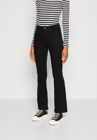 Jeans hitam bercelah yang terbuat dari denim, menampilkan pinggang yang pas dan jahitan halus. Dipadukan dengan baju lengan panjang bergaris hitam dan putih.