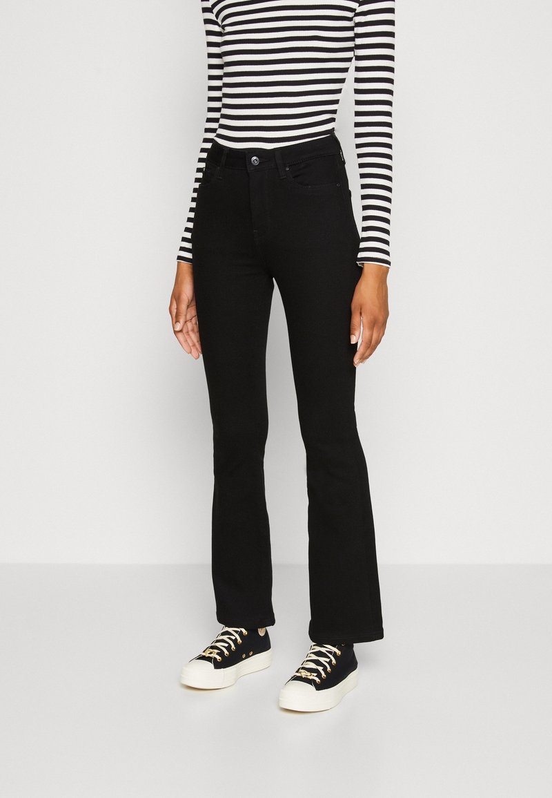 Jeans hitam bercelah yang terbuat dari denim, menampilkan pinggang yang pas dan jahitan halus. Dipadukan dengan baju lengan panjang bergaris hitam dan putih.