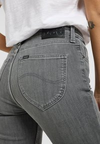 Grijze denim jeans met een aansluitend ontwerp, met een kenmerkende vorm van de achterzak en een zwart merklabel op de tailleband.