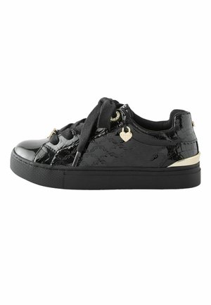 Schwarzer Sneaker aus Lackleder mit dicker Sohle, breiten schwarzen Schnürsenkeln, goldenem herzförmigem Anhänger und goldenem Akzent an der Ferse.