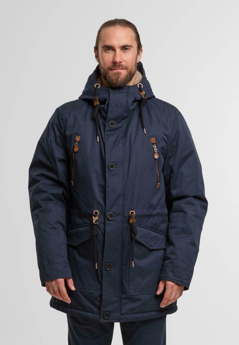 Navy blue parka with a hood, featuring brown leather accents, drawstrings, large front pockets, and a button-up closure. Textured fabric.