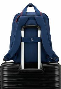 Zaino navy con spallacci regolabili appoggiato su una valigia rigida nera, dotata di manico telescopico e superficie testurizzata. Hardware standard.