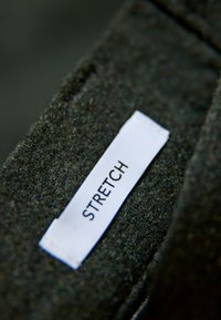 Tejido negro texturizado con una etiqueta blanca prominente que dice "STRETCH". El tejido parece suave y ligeramente peludo.